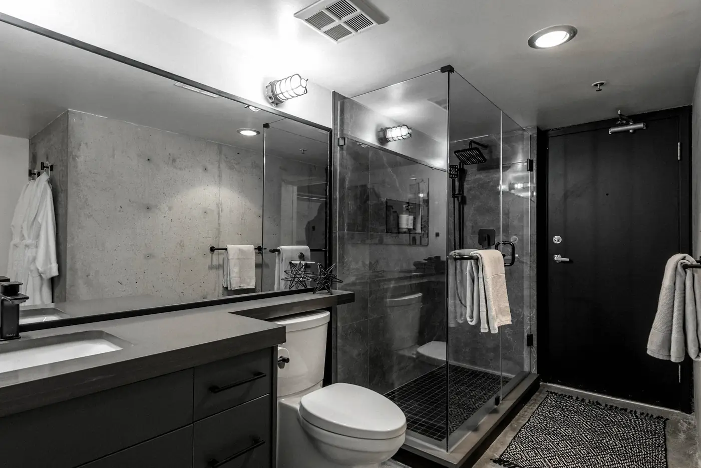 Douche vitrée, meuble vasque gris foncé et murs couleur béton