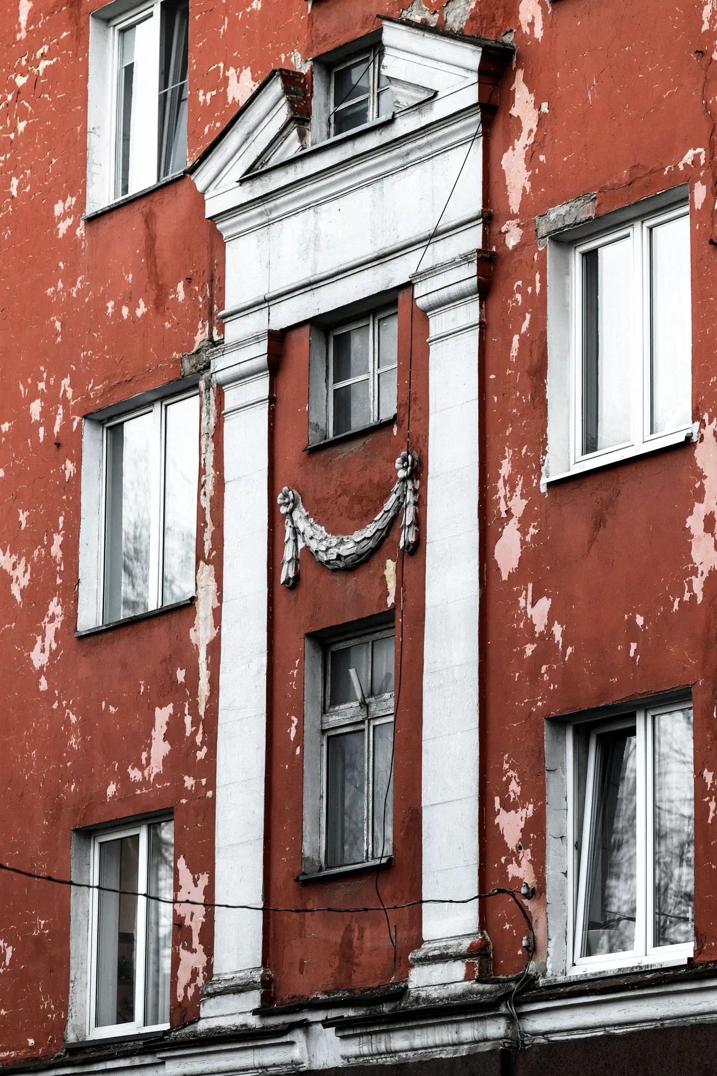 Façade rouge dont la peinture s’écaille, encadrements moulurés blancs