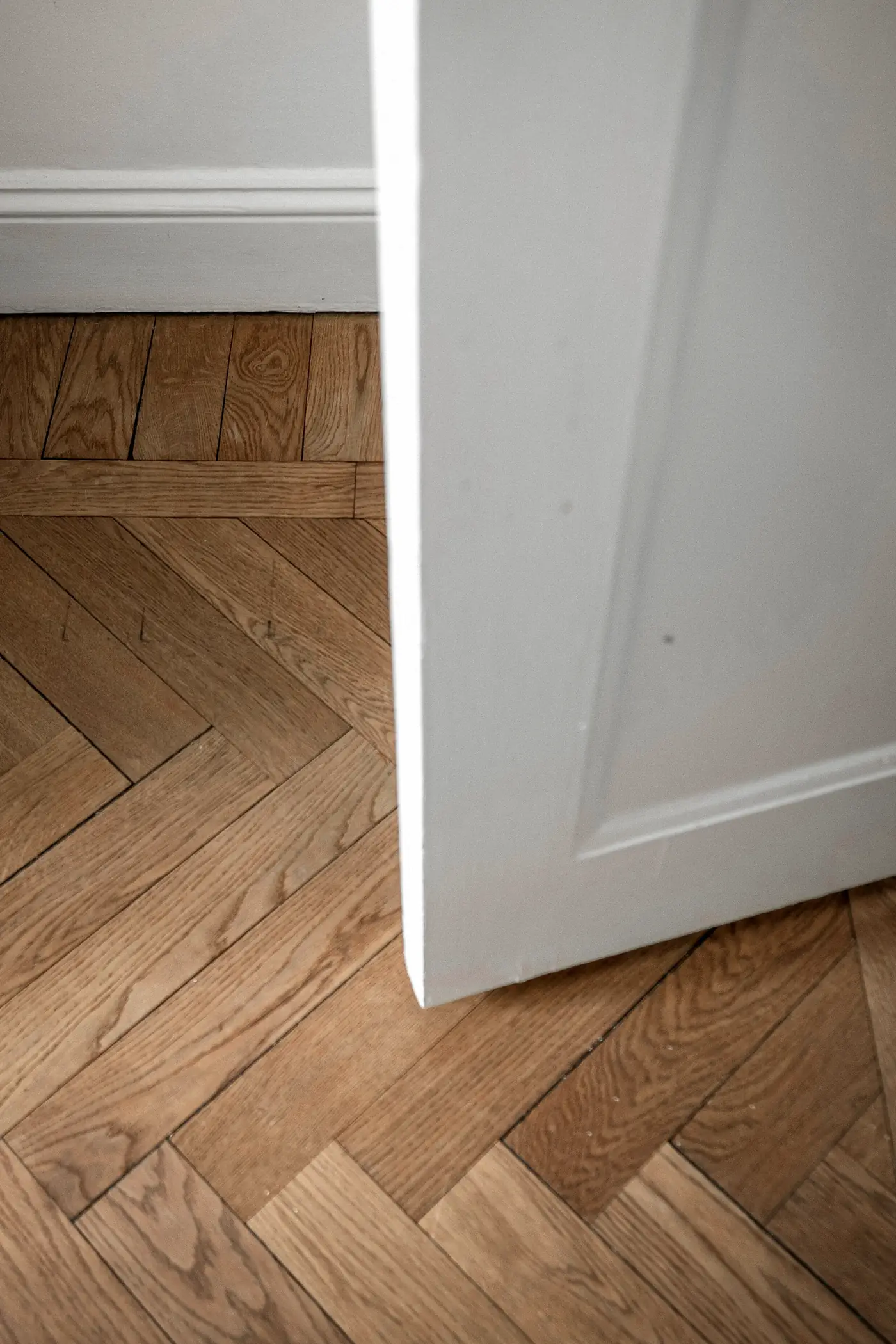 Porte blanche ouverte sur un parquet à chevrons